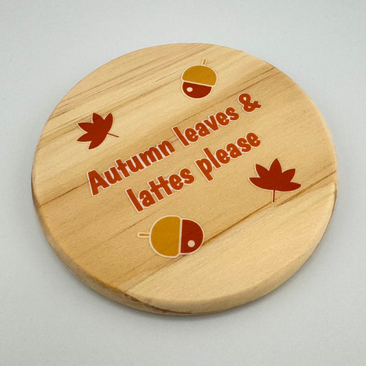 Wooden coaster with 'Autumn leaves & lattes please' text and leaf designs on a light gray background