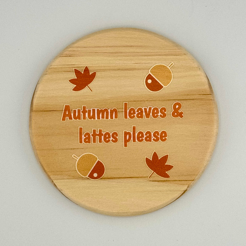 Wooden coaster with autumn-themed design and text on a light gray background