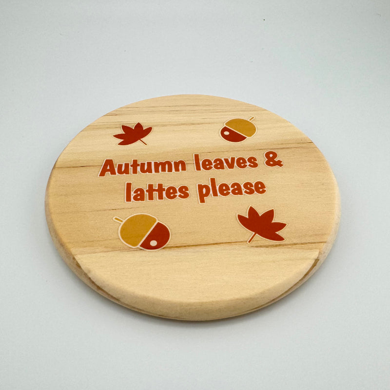 Wooden coaster with autumn-themed design and text on a light gray background